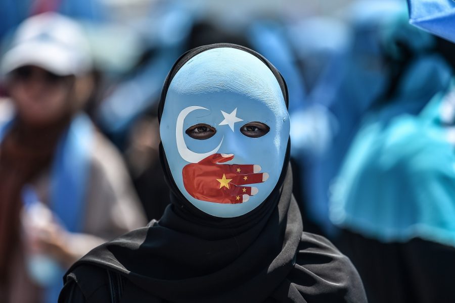 TOPSHOT+-+A+demonstrator+wearing+a+mask+painted+with+the+colours+of+the+flag+of+East+Turkestan+and+a+hand+bearing+the+colours+of+the+Chinese+flag+attends+a+protest+of+supporters+of+the+mostly+Muslim+Uighur+minority+and+Turkish+nationalists+to+denounce+Chinas+treatment+of+ethnic+Uighur+Muslims+during+a+deadly+riot+in+July+2009+in+Urumqi%2C+in+front+of+the+Chinese+consulate+in+Istanbul%2C+on+July+5%2C+2018.+-+Nearly+200+people+died+during+a+series+of+violent+riots+that+broke+out+on+July+5%2C+2009+over+several+days+in+Urumqi%2C+the+capital+city+of+the+Xinjiang+Uyghur+Autonomous+Region%2C+in+northwestern+China%2C+between+Uyghurs+and+Han+people.+%28Photo+by+OZAN+KOSE+%2F+AFP%29++++++++%28Photo+credit+should+read+OZAN+KOSE%2FAFP%2FGetty+Images%29
